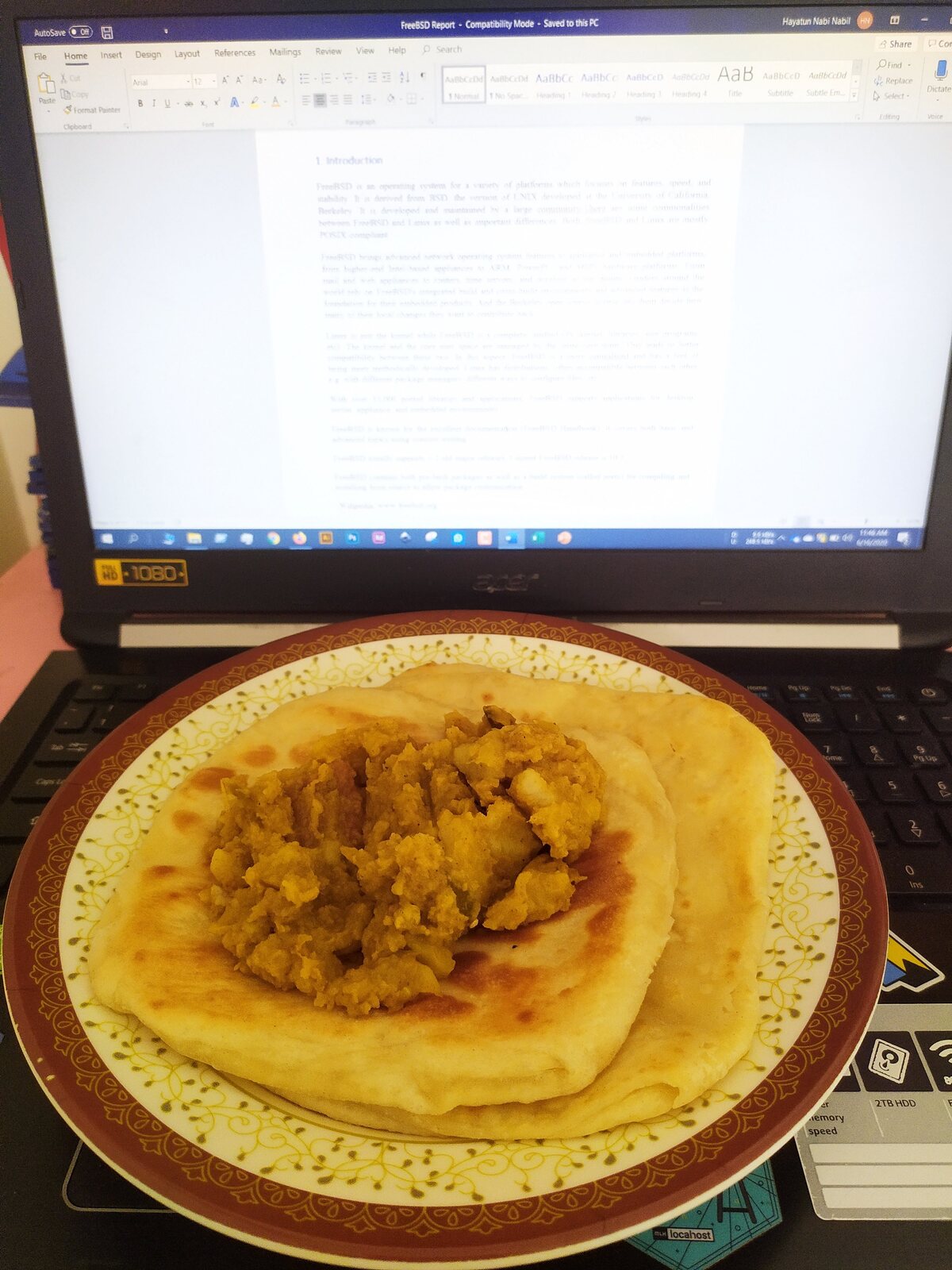A laptop showing a blank document next to a plate with a pancake.