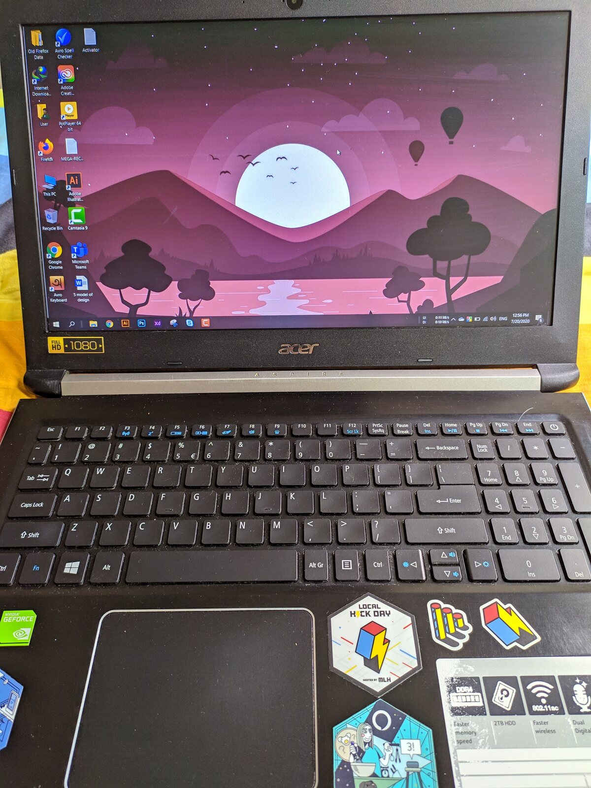 A laptop showing a colourful mountain wallpaper with stickers on the palm rest.