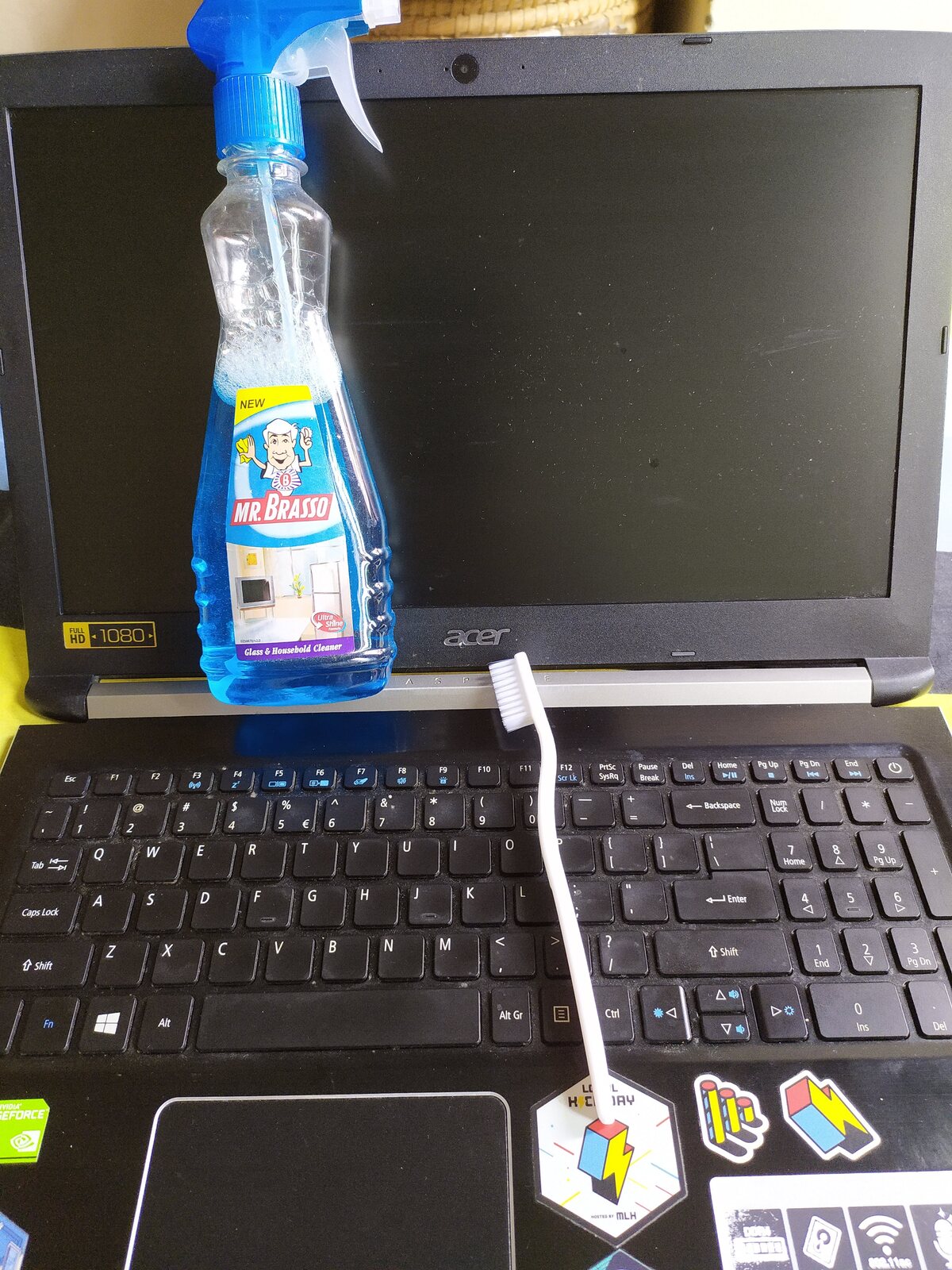 A laptop on a colourful sheet with a spray bottle for cleaning.