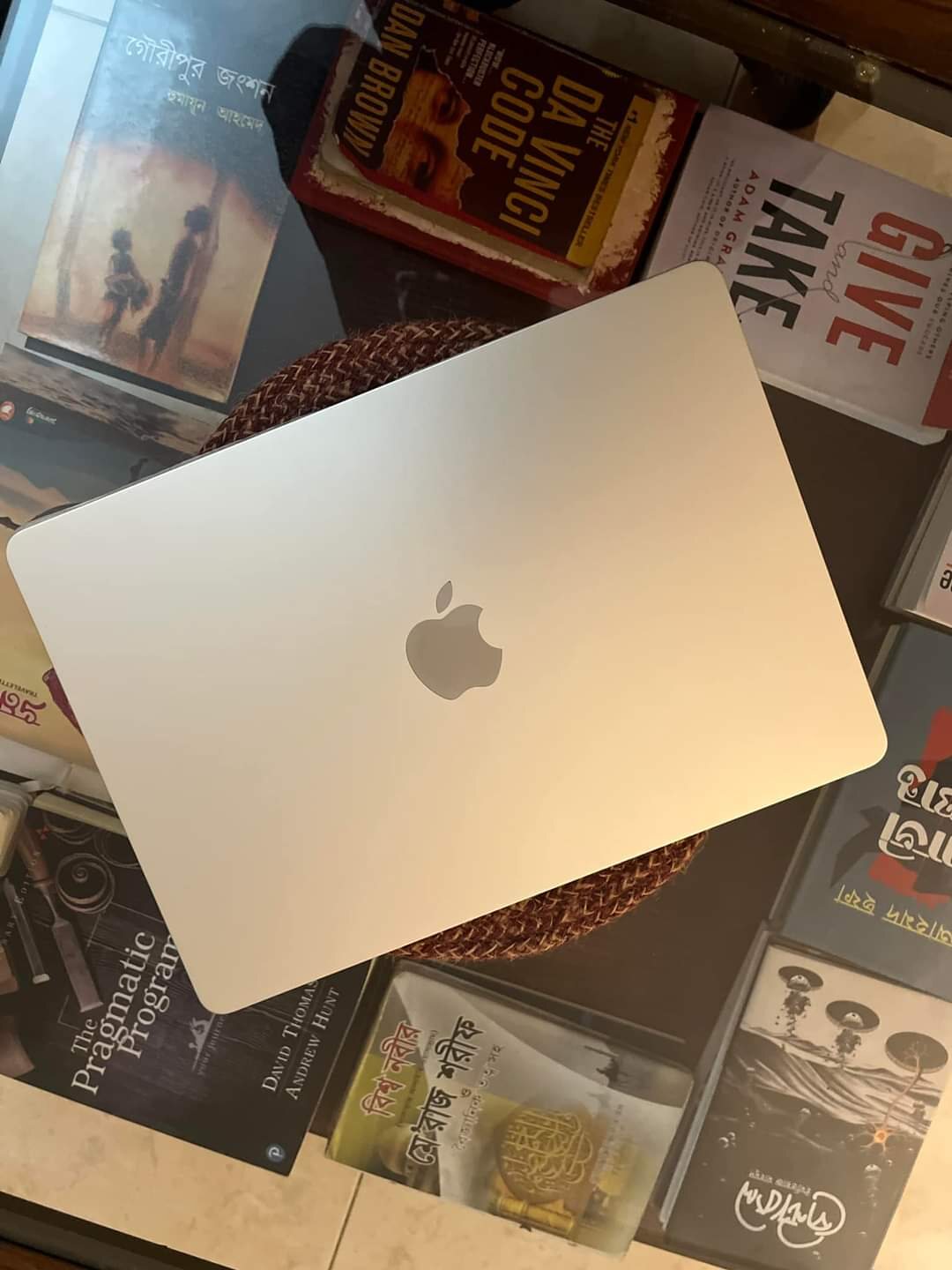 A new silver MacBook resting on its box on top of a stack of books.